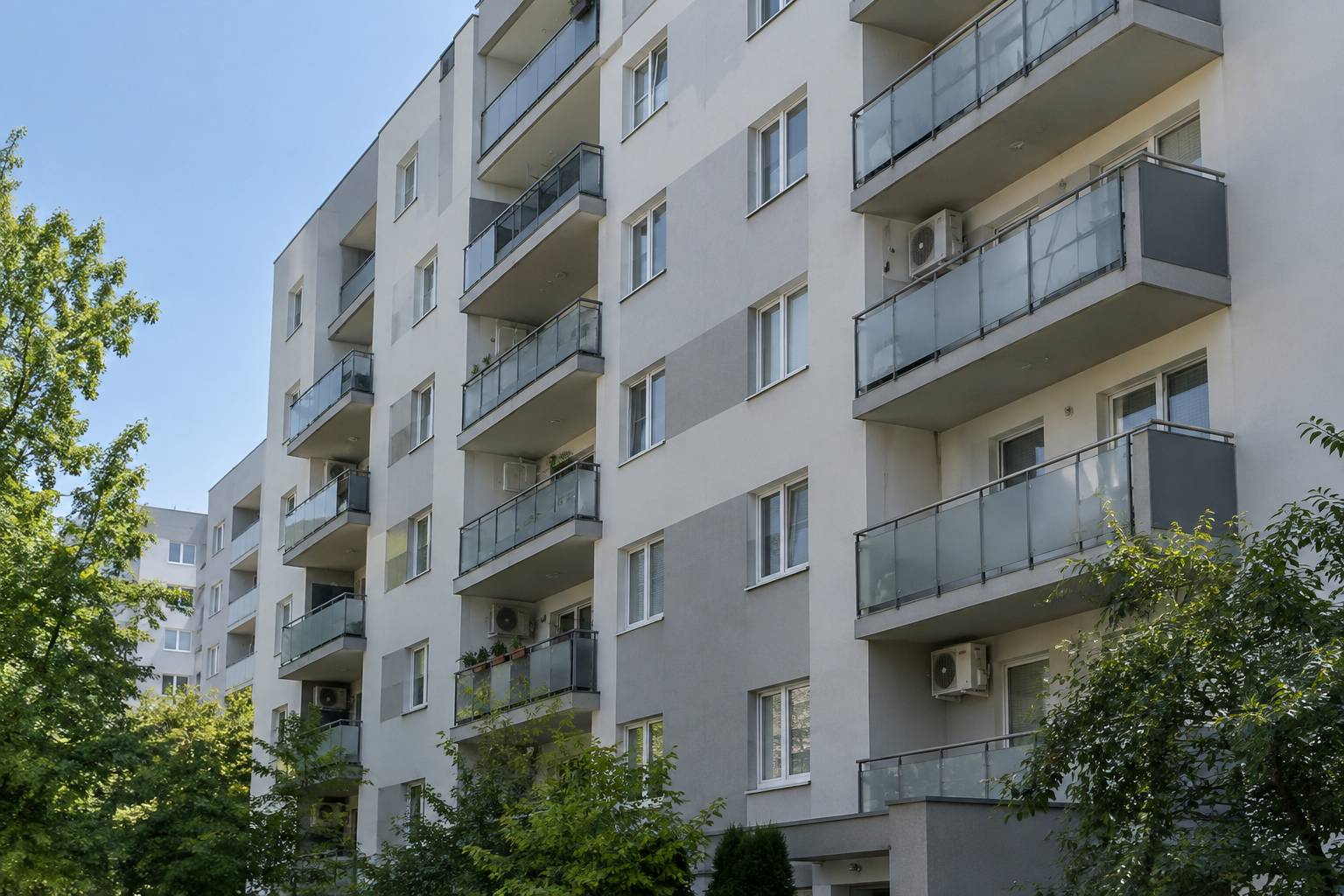 Elewacja bloku mieszkalnego z balkonami i kilkoma jednostkami zewnętrznymi klimatyzacji zamontowanymi na wspornikach
