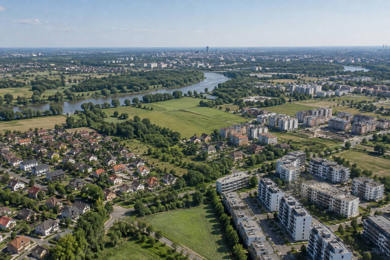 Widok z lotu ptaka na osiedla, domy jednorodzinne i pola na obrzeżach miasta z rzeką w tle